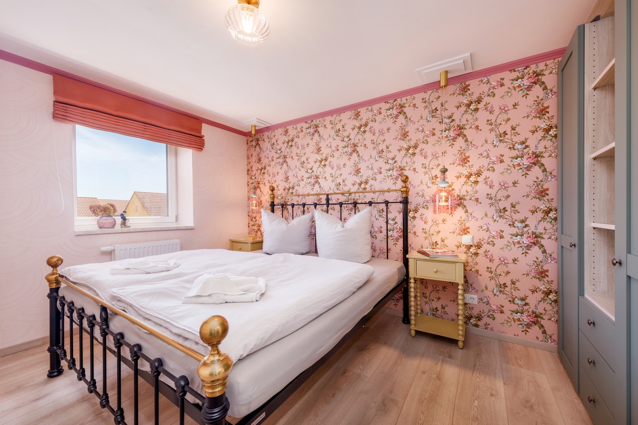 Fewo „Rosenwald am Meer“ Haus Meergold in Sassnitz auf der Insel Rügen - 2-Zimmer-Ferienwohnung Rosen am Meer - Schlafzimmer im Boutique-Stil mit Rosentapeten und Eisenbett und Kleiderschrank