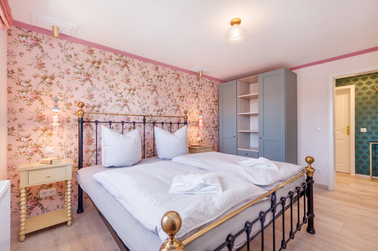 Fewo „Rosenwald am Meer“ Haus Meergold in Sassnitz auf der Insel Rügen - 2-Zimmer-Ferienwohnung Rosen am Meer - Schlafzimmer im Boutik-Stil mit Mustertapeten, Metallbett, grossem Kleiderschrank und Verdunkelungsmöglichkeit
